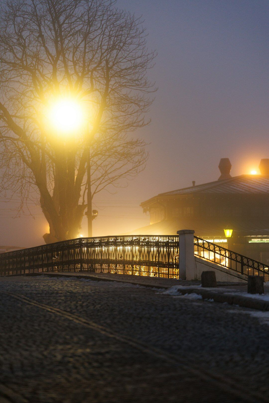 Foggy cobblestone street with a glowing lamppost at night